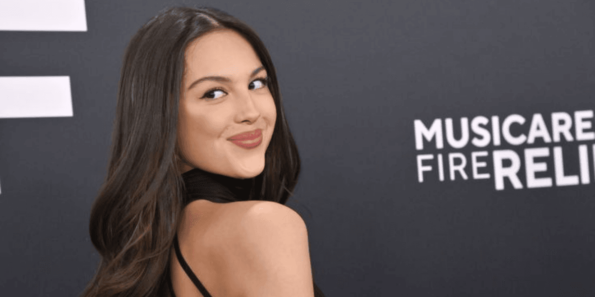 Young woman in black dress poses playfully against a dark backdrop with event branding