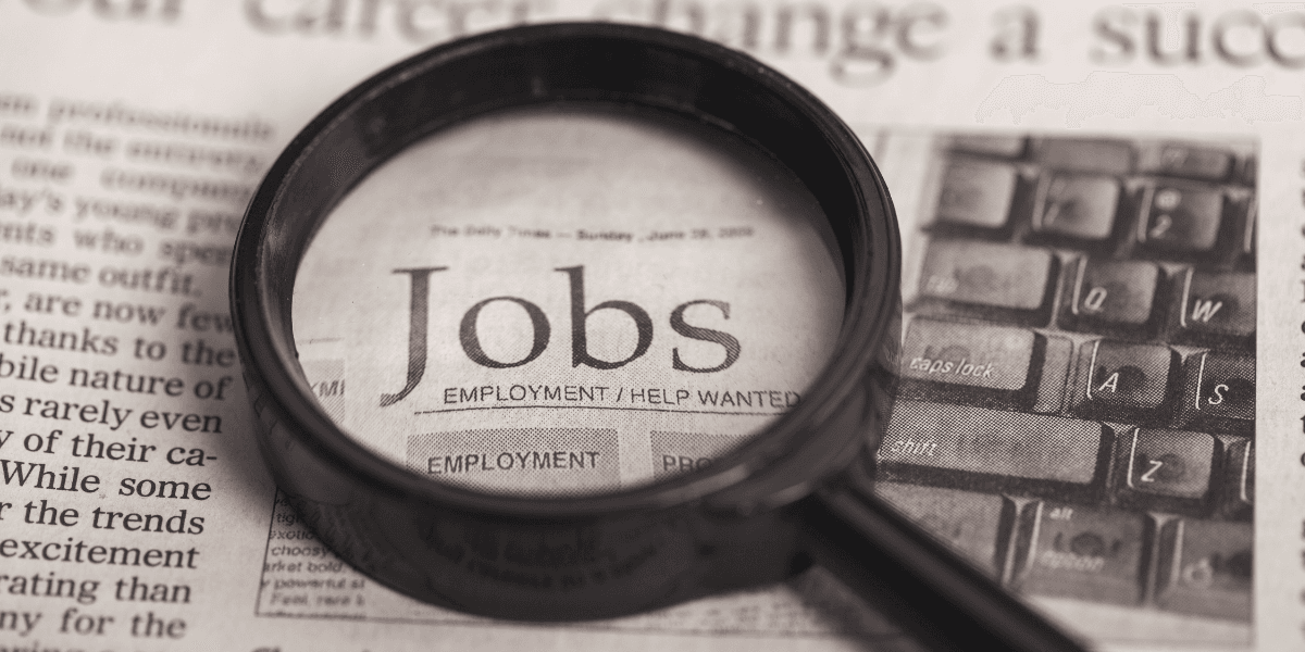 Magnifying glass over a newspaper page highlighting job listings and employment opportunities