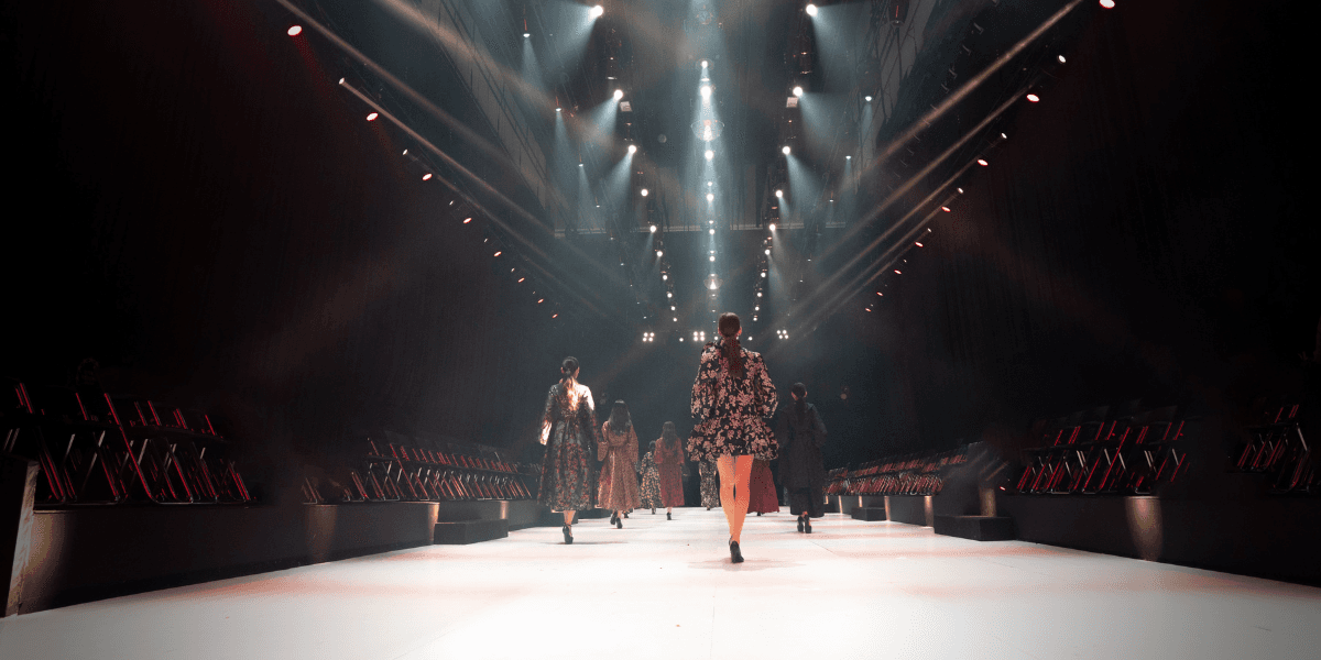 Fashion models walking down a brightly lit runway with empty audience seats