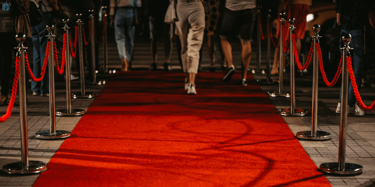 People walking down a red carpet lined with shiny stanchions and ropes