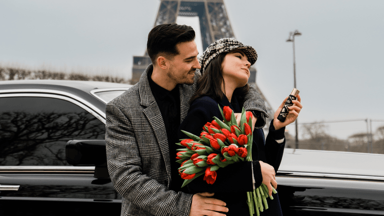 "A couple embraces in front of a luxurious car, holding tulips with the Eiffel Tower in the background."