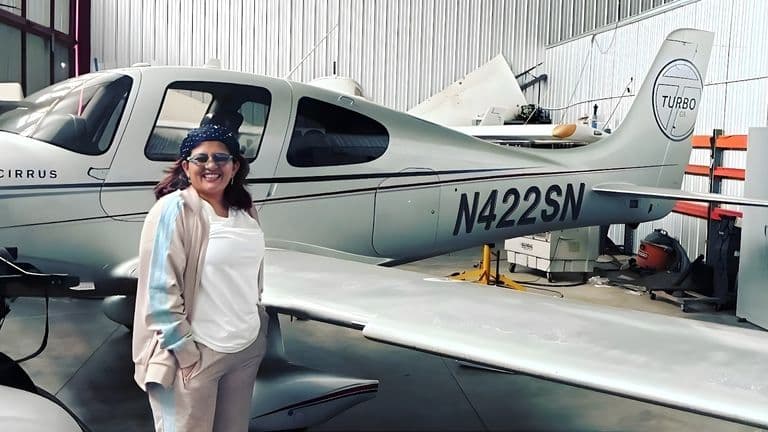 Isha Chhabra, President of GlobalGlowFilms, standing beside a Cirrus aircraft, embodying the brand's global lifestyle ethos.