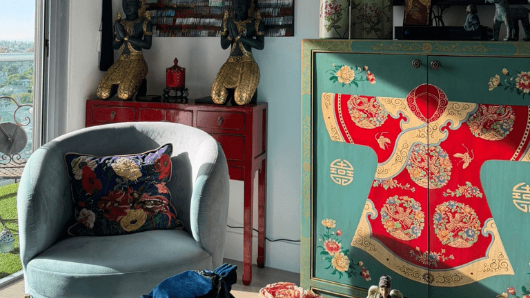 Eclectic living room with Asian decor, teal armchair, red cabinet, and ornate painted cabinet near balcony view.