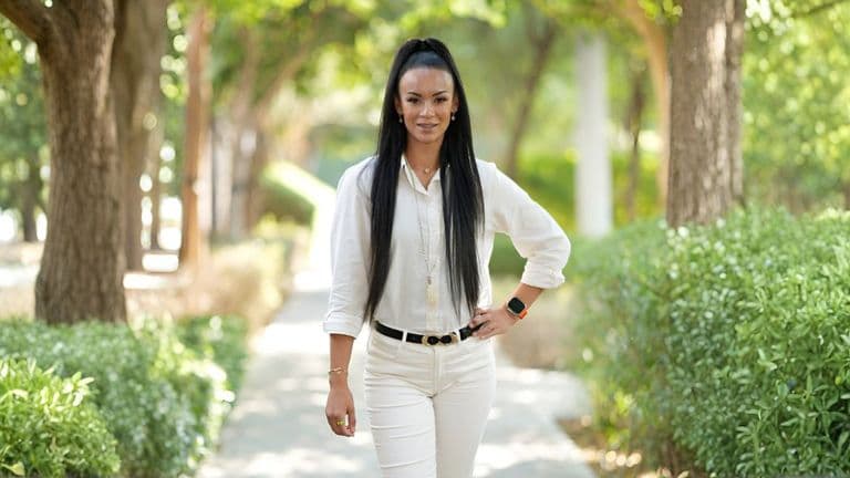 Dubai-based holistic coach Caroline Bakker walks confidently along a tree-lined path, wearing all white, symbolizing peace, healing, and empowerment.
