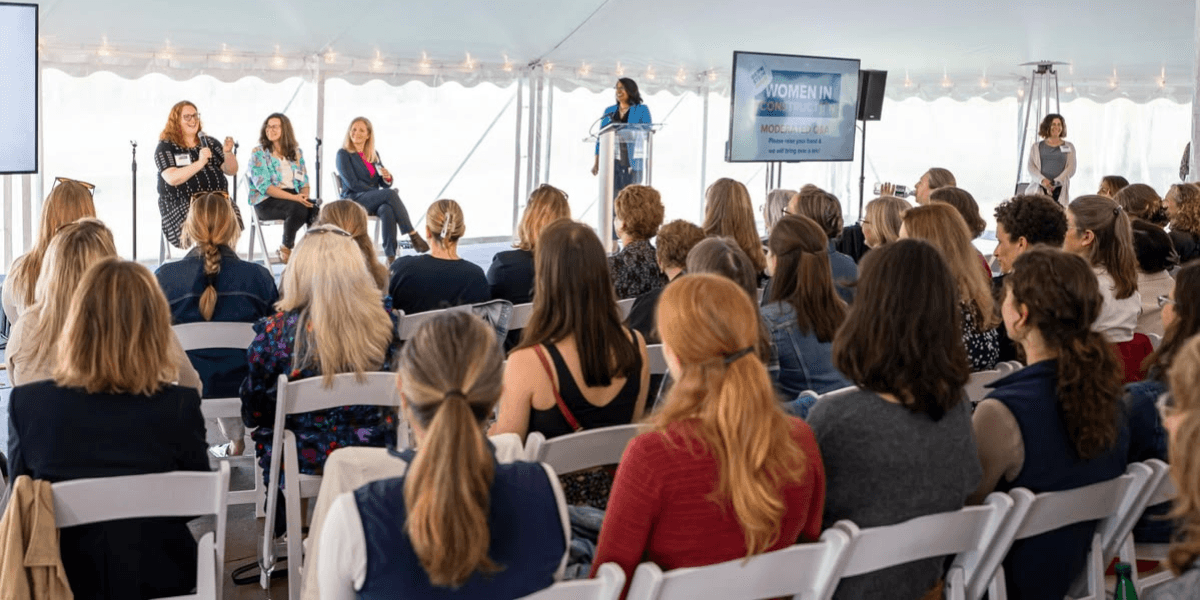 Audience at a women’s conference listening to speakers on stage under a tent