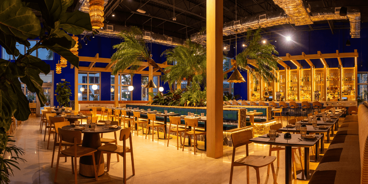 Modern restaurant interior with wooden furniture, tropical plants, and warm lighting