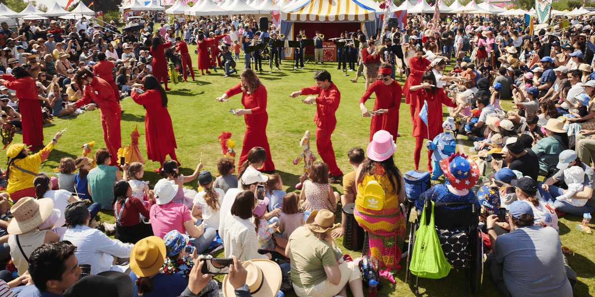 A vibrant outdoor festival scene with a crowd watching dancers in red attire.