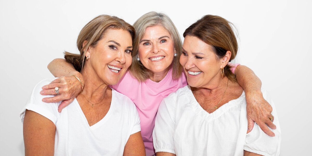 Three women smiling together, representing confidence, inclusivity, and accessible beauty.