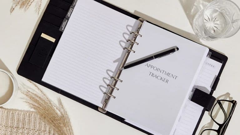 a neatly organized planner with the title "APPOINTMENT TRACKER," a pen, glasses, and a candle.