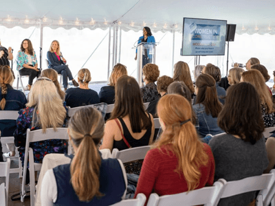 Audience at a women’s conference listening to speakers on stage under a tent