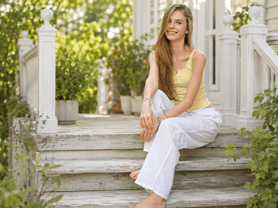 Smiling woman in yellow tank top sitting on wooden steps surrounded by greenery