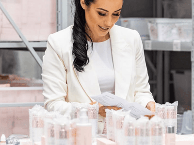 Woman in a white blazer reviewing paperwork amid beauty product packaging on a table