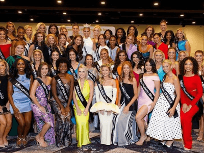 Group photo of contestants in evening gowns at a pageant event on stage