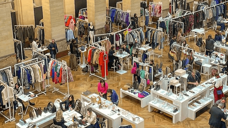 A bustling fashion exhibition featuring various clothing and accessory displays with attendees shopping.