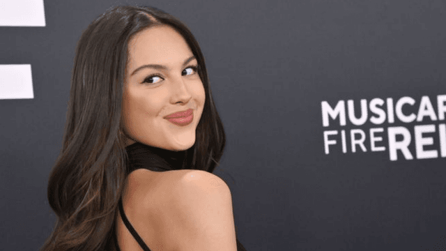 Young woman in black dress poses playfully against a dark backdrop with event branding