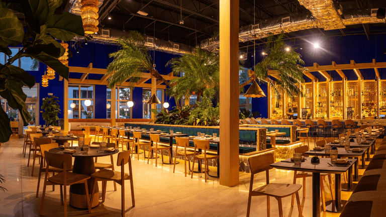 Modern restaurant interior with wooden furniture, tropical plants, and warm lighting