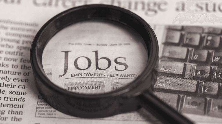 Magnifying glass over a newspaper page highlighting job listings and employment opportunities