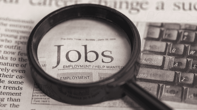 Magnifying glass over a newspaper page highlighting job listings and employment opportunities