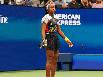 A young female tennis player stands on the court, looking frustrated during a match