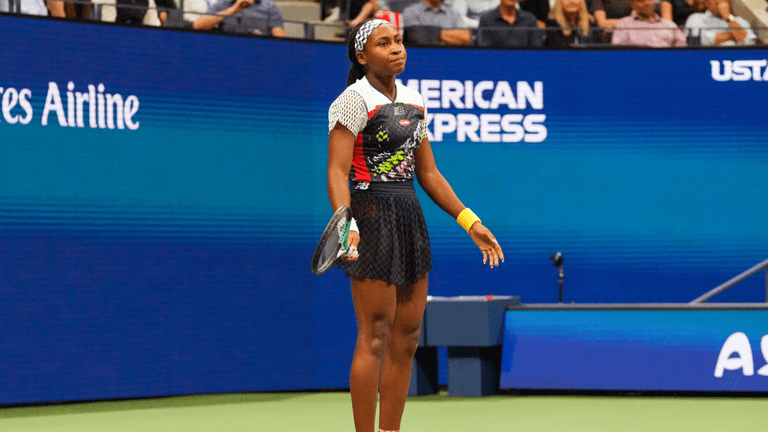 A young female tennis player stands on the court, looking frustrated during a match
