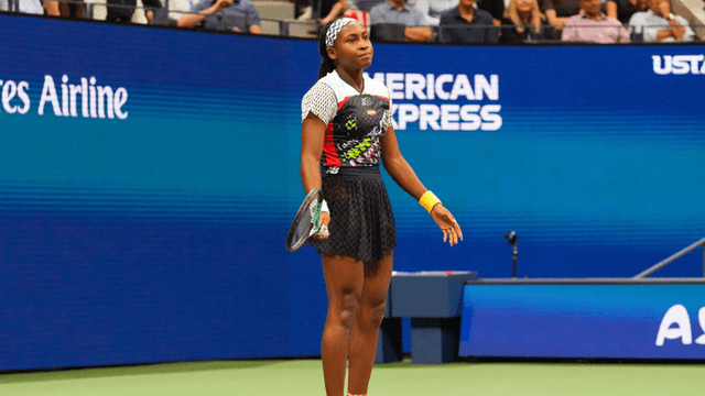 A young female tennis player stands on the court, looking frustrated during a match