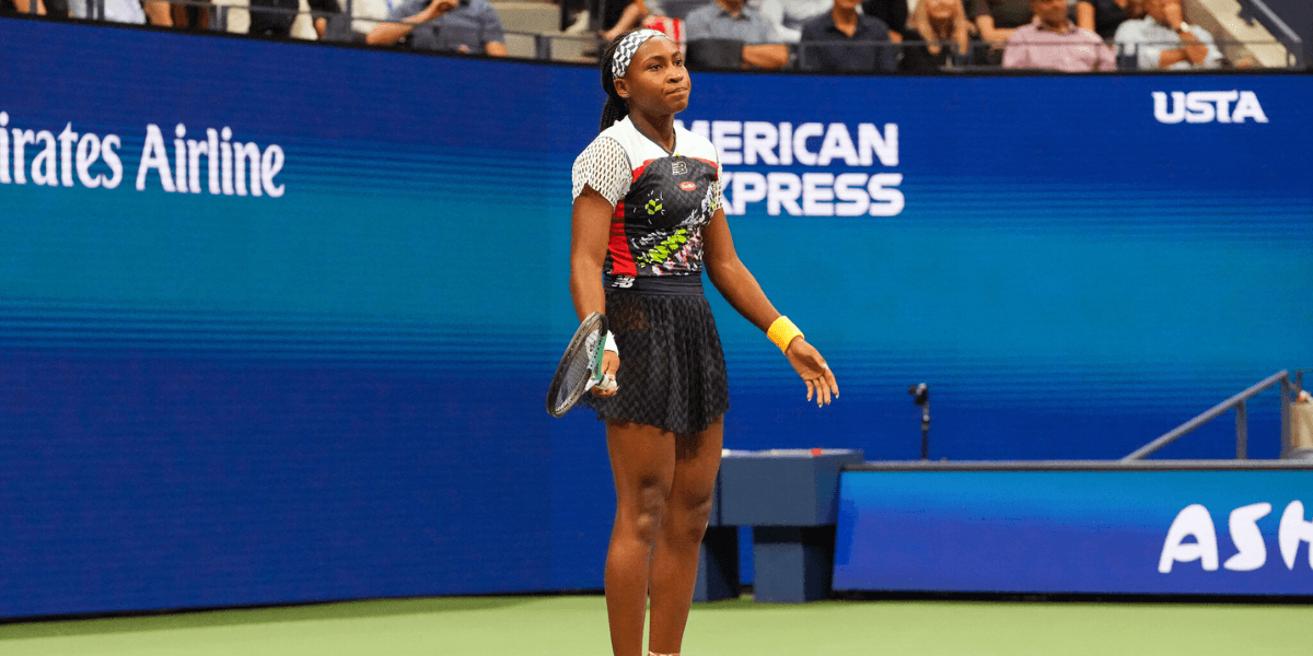 A young female tennis player stands on the court, looking frustrated during a match