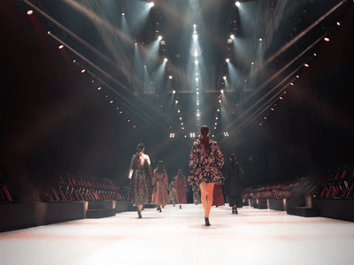 Fashion models walking down a brightly lit runway with empty audience seats