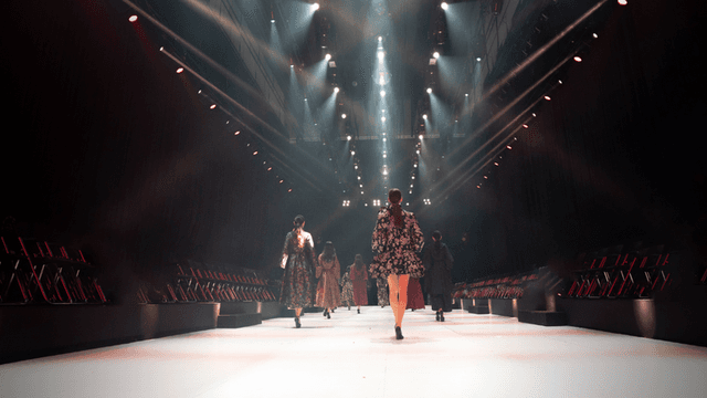 Fashion models walking down a brightly lit runway with empty audience seats