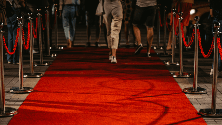 People walking down a red carpet lined with shiny stanchions and ropes