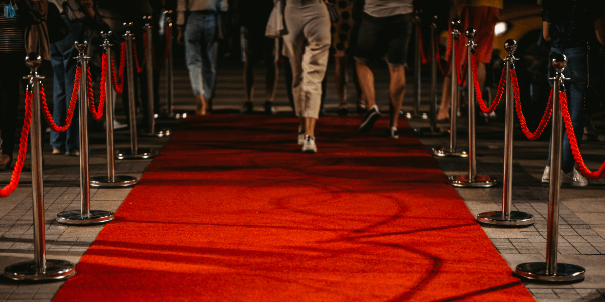 People walking down a red carpet lined with shiny stanchions and ropes