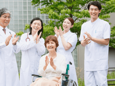 A smiling elderly woman in a wheelchair is cheered on by four medical staff members