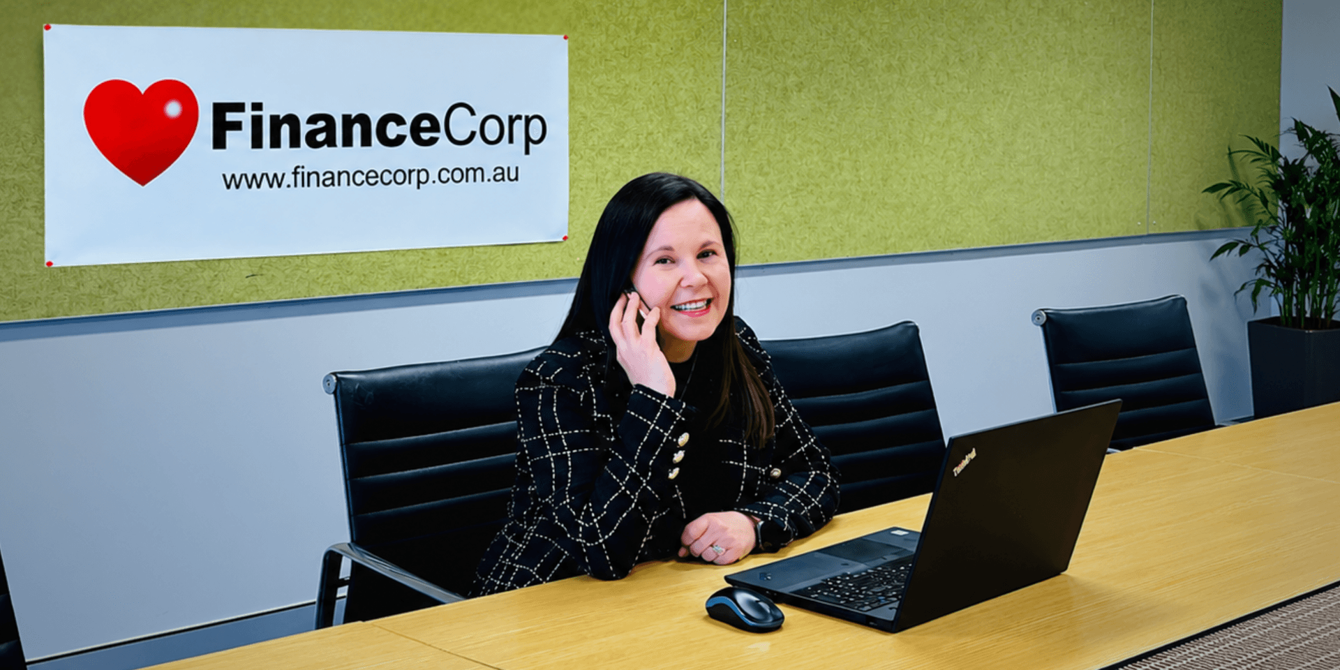 Woman talking on the phone seated at a desk with a laptop and company banner