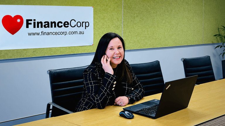 Woman talking on the phone seated at a desk with a laptop and company banner