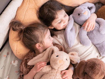 Two young girls cuddle with plush toys on a cozy bed.