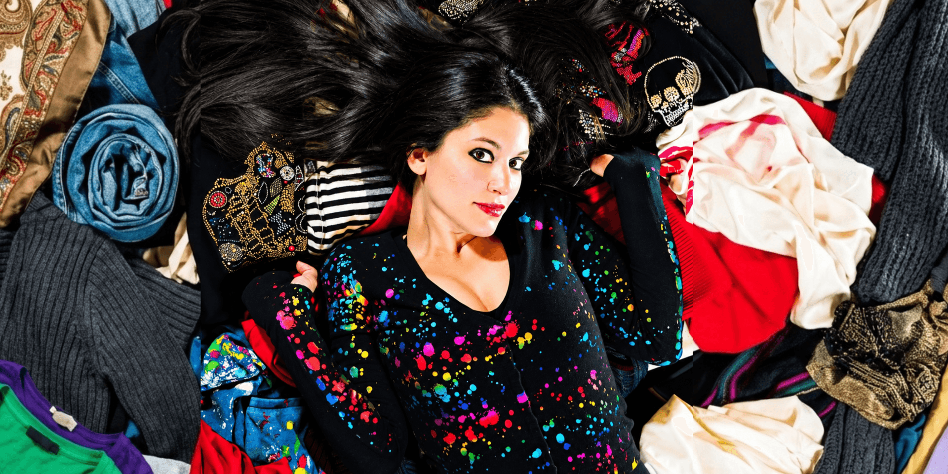 Woman lying on colorful clothing, surrounded by various fabric patterns and textures