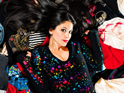 Woman lying on colorful clothing, surrounded by various fabric patterns and textures