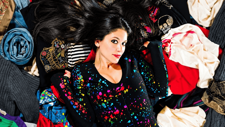 Woman lying on colorful clothing, surrounded by various fabric patterns and textures