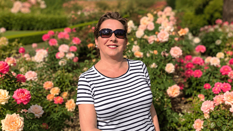 Woman in sunglasses poses among blooming roses in a vibrant garden setting