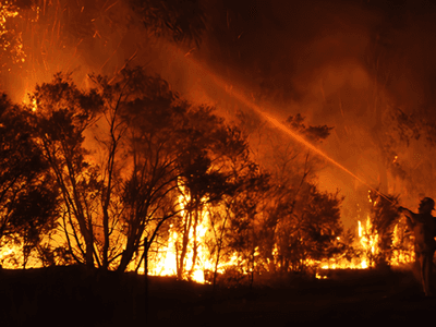 Firefighters battling a large wildfire amidst towering flames and thick smoke at night