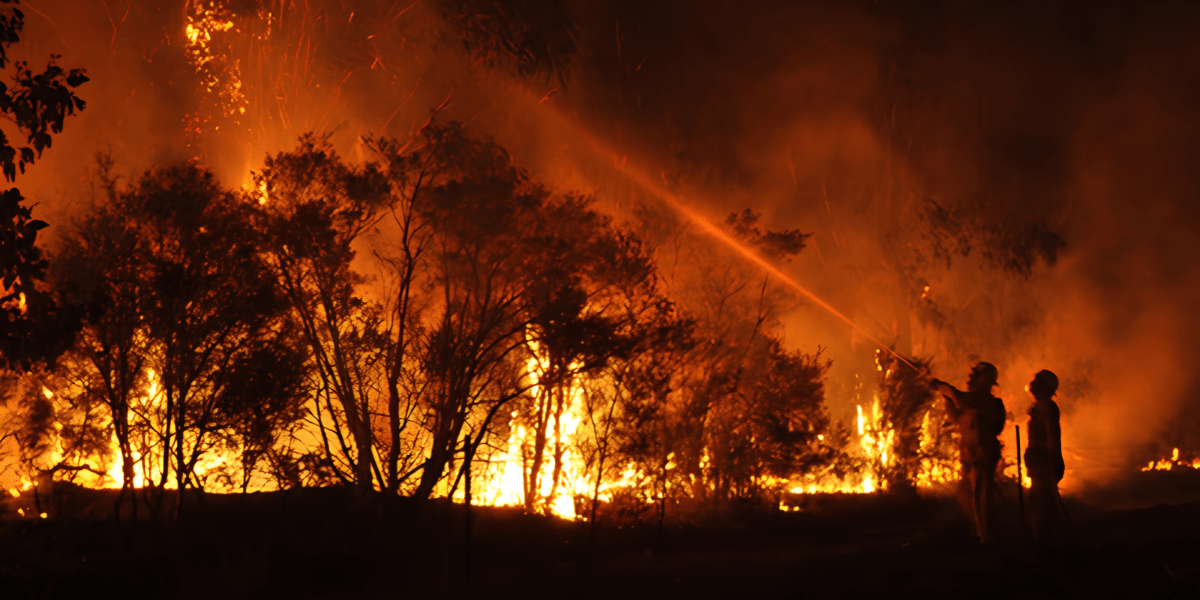 Firefighters battling a large wildfire amidst towering flames and thick smoke at night