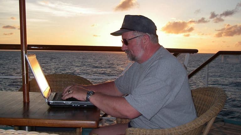 Baer Charlton writing on a laptop aboard a ship at sunset.
