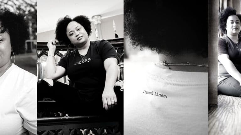 A woman with afro hair sits on a chair, wearing a minimalist tee from Literal Lines., embodying authentic storytelling.