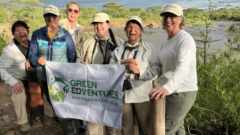Women holding the Green Edventures flag in front of Tanzania’s natural landscape.