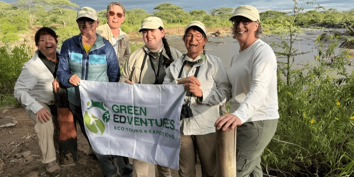 Women holding the Green Edventures flag in front of Tanzania’s natural landscape.