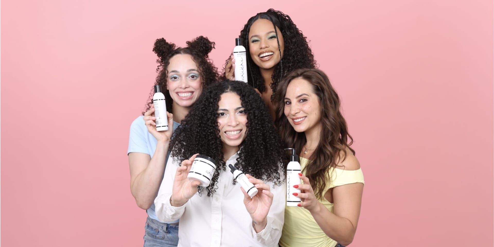 Four women with textured hair display Cricri Curls products together against a pink background, celebrating inclusive clean beauty.