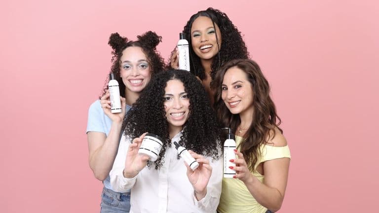 Four women with textured hair display Cricri Curls products together against a pink background, celebrating inclusive clean beauty.