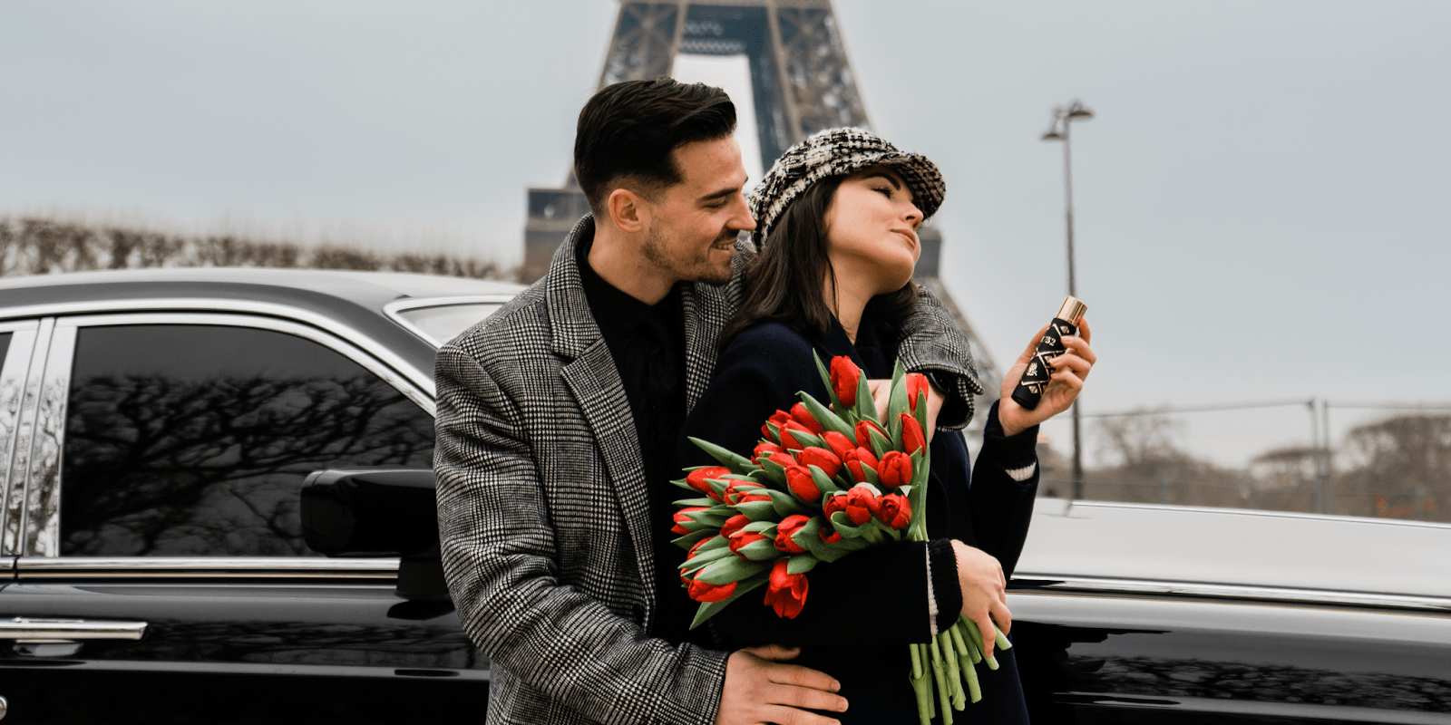 "A couple embraces in front of a luxurious car, holding tulips with the Eiffel Tower in the background."