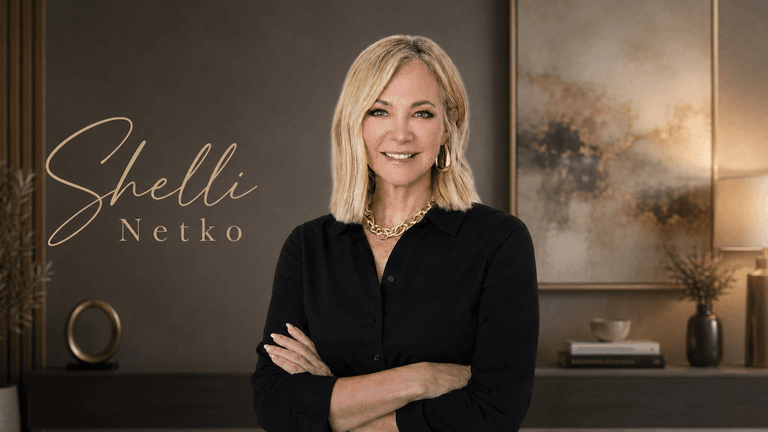 Professional portrait of blonde woman in black blouse, arms crossed, with elegant office backdrop and name logo.