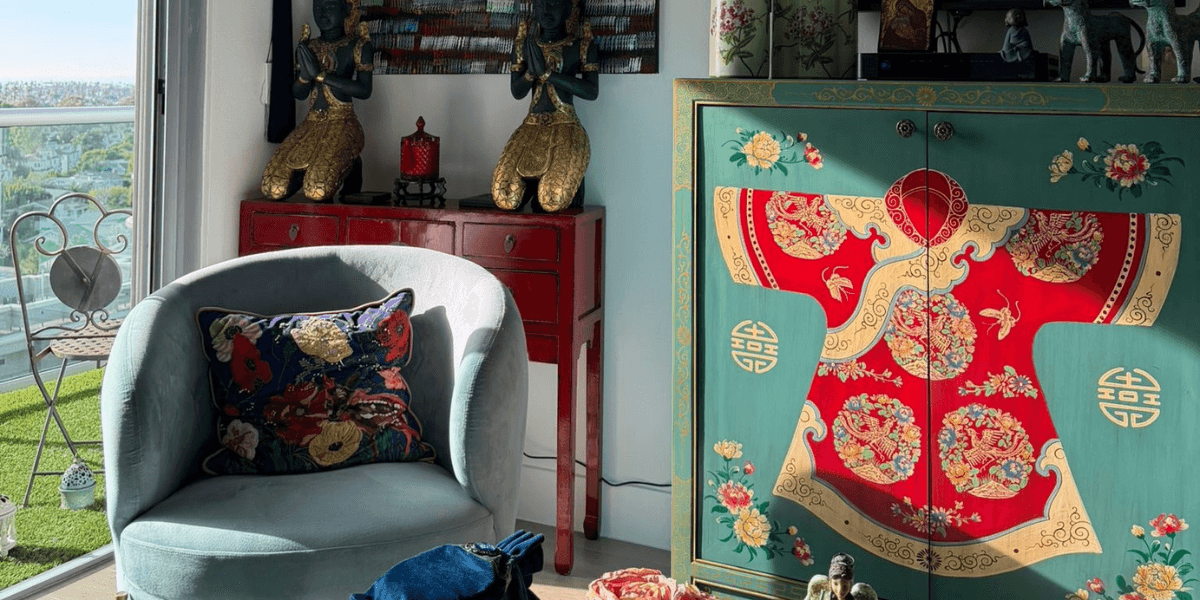 Eclectic living room with Asian decor, teal armchair, red cabinet, and ornate painted cabinet near balcony view.