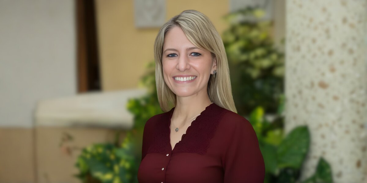 A woman with blonde hair wearing a maroon shirt, smiling and embodying creativity and inspiration for children’s adventures.
